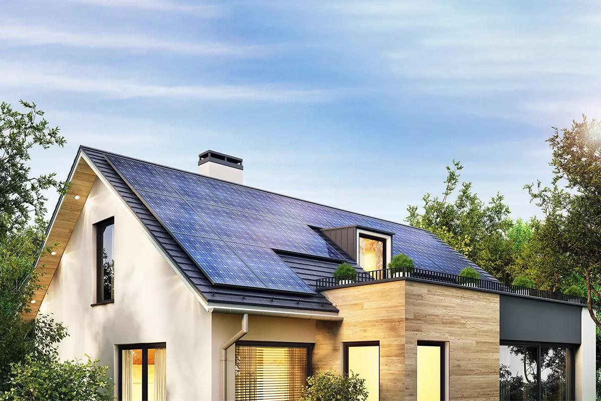 Modern single-family house with rooftop solar panels, large windows, and surrounding trees under a clear blue sky.